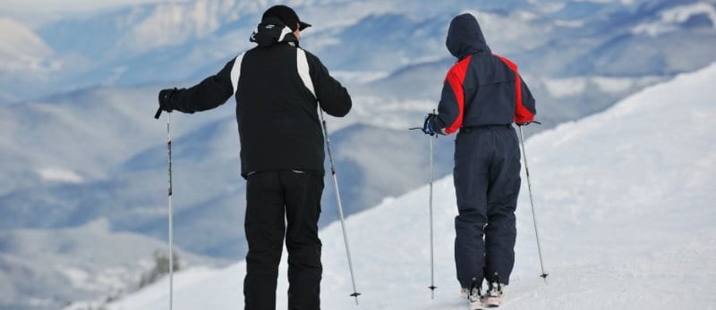 two people with skis looking over a mountain two people with skis looking over a mountain